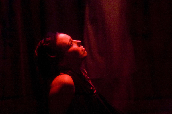 a woman, seen in profile, looks upwards, bathed in red light, in a dark environment