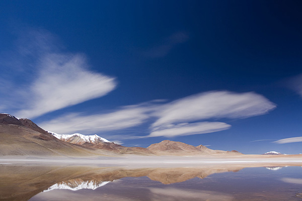 mountains on the horizon, reflected in the lake ahead, under a blue sky, in the Bolivian highlands.